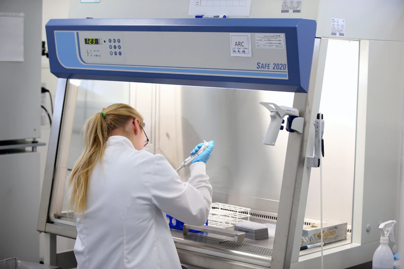 Scientist sat under fume hood with pipette 