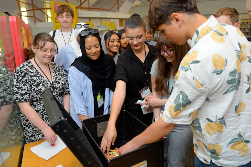 A group of students gathered around a table selecting a prize from a large box after completing a Step Up summer school activity.