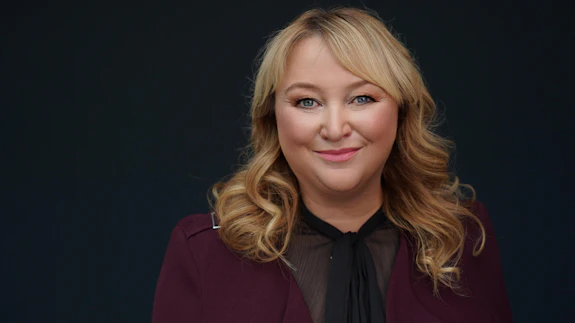 A woman is photographed wearing a suit against a black background.