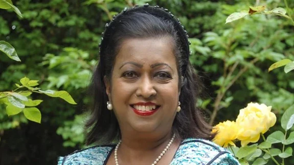 A woman is photographed wearing a suit jacket against a background of rose bushes.
