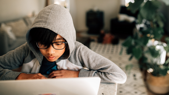 Young boy with his hood up using a laptop at home