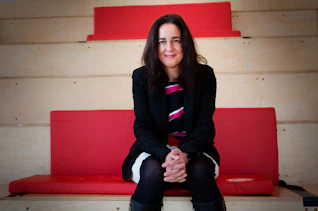A woman sat down on wooden steps with red cushions, smiling directly into the camera lens.
