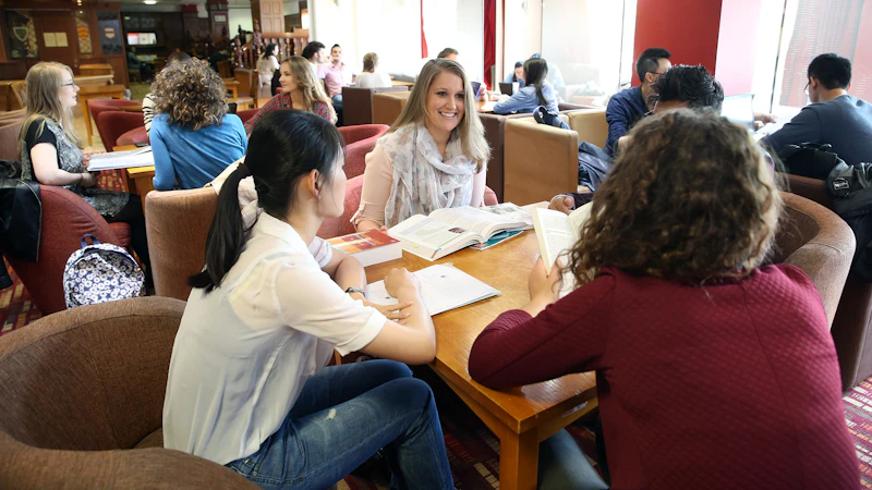 Four students sitting around a table in a crowded room.