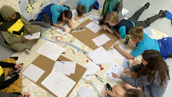 Children sit on the floor in a circle and draw pictures whilst looking at a map of Cardiff