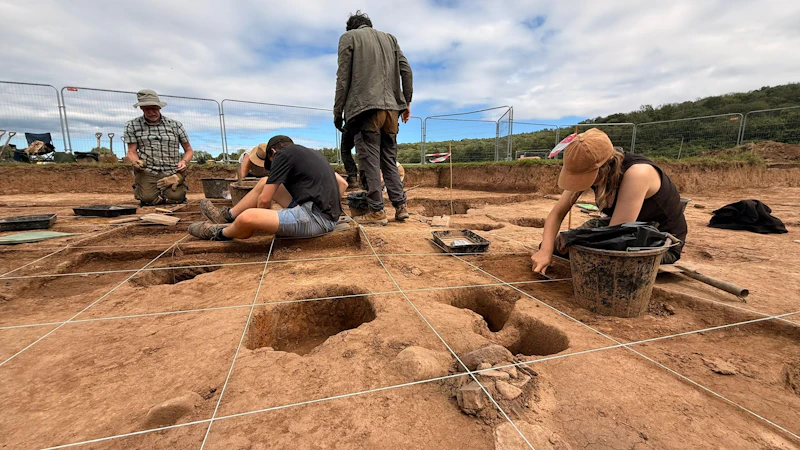 Low-angle shot of a group of people using tools to excavate an archaeological dig site.