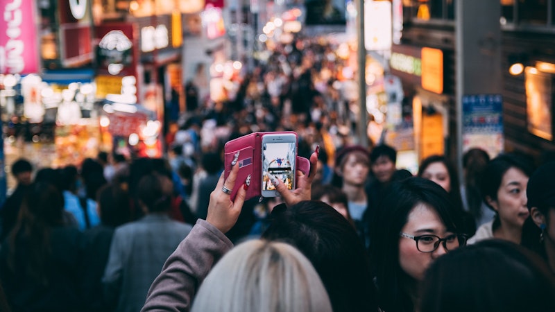 A woman taking a photo on her mobile phone in a crowded street.